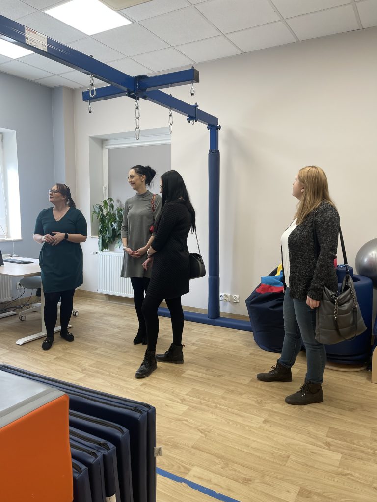 Na zdjęciu Koordynator Punktu Panią Justynę Syroka i pracownicy MOPR Chełm w Sali terapii SI. Pani Justyna wskazuje na znajdujące się pod ścianą pomoce i zabawki terapeutyczne