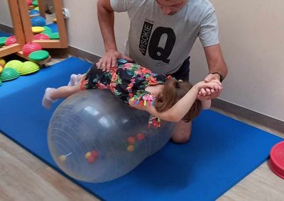 Zajęcia rehabilitacyjne na piłce. Rehabilant wykonuje ćwiczenia usprawniające z uczestniczką zajęć